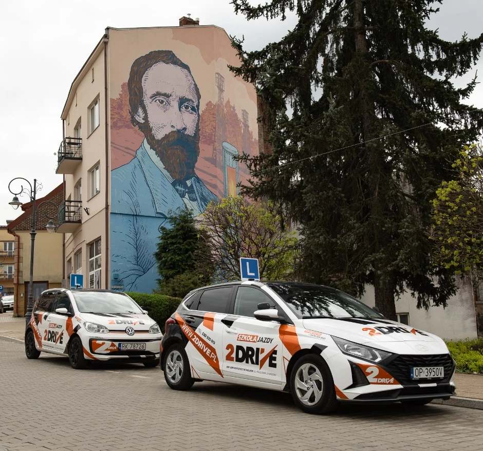 Samochody szkoleniowe 2Drive na tle muralu w Krośnie – kurs prawa jazdy kat. B